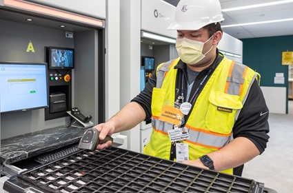 A pharmacy manager in a safety vest and hard hat, using a handheld scanner, participates in a “dress rehearsal” at the Pavilion.